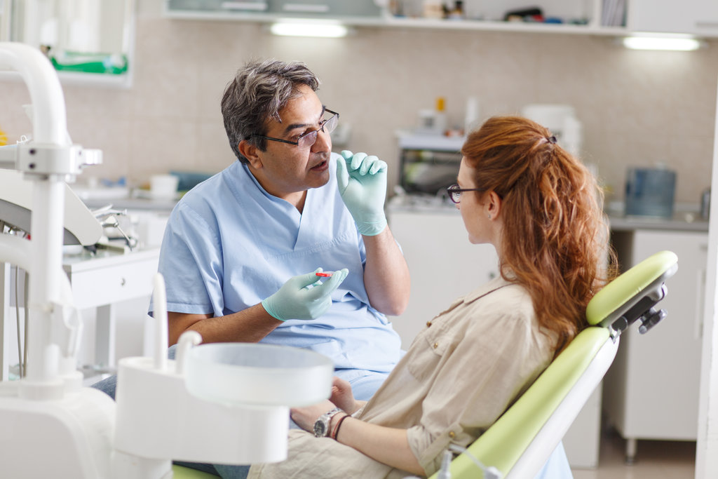 A professional dentist, equipped with a bright smile, converses with his red-haired female patient, carefully explaining the upcoming treatment, and ensuring her comfort throughout the process.