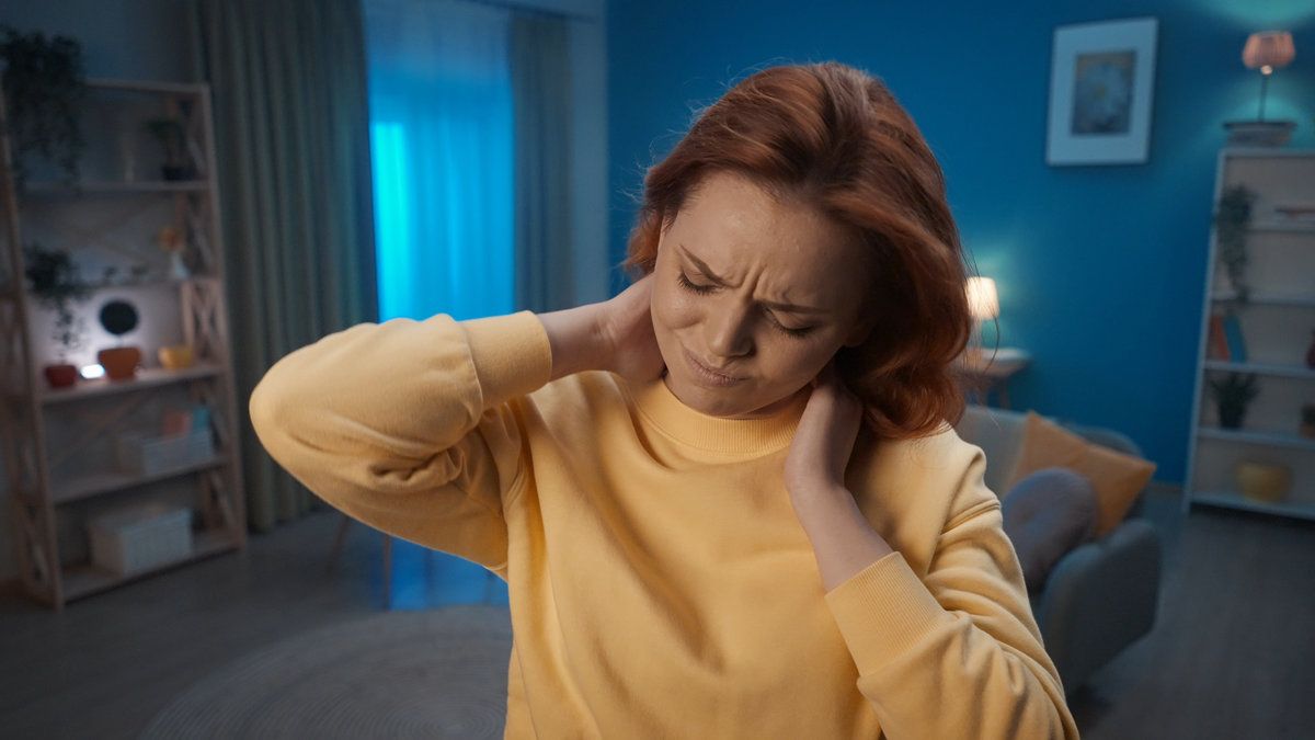 Tired woman with a painful expression is holding her neck close up. Incorrect posture, pain in the neck, shoulders, joints. Home medicine concept.
