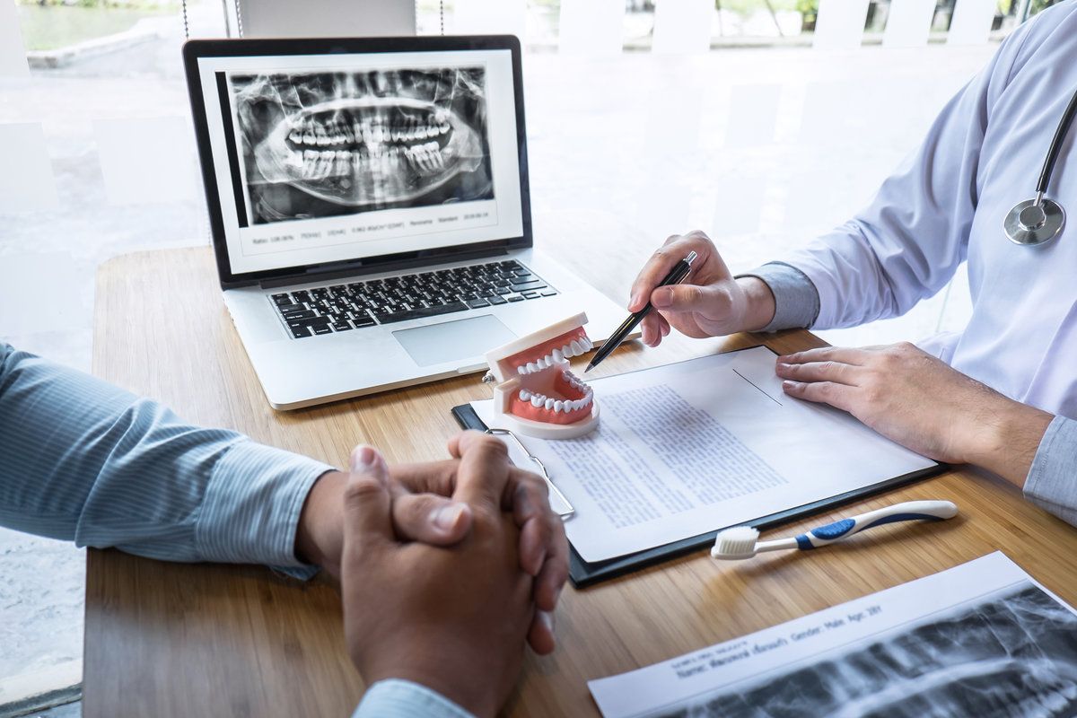 Professional Dentist showing jaw and teeth the x-ray photograph and discussing during explaining the consultation treatment issues with patient and writing history list on report